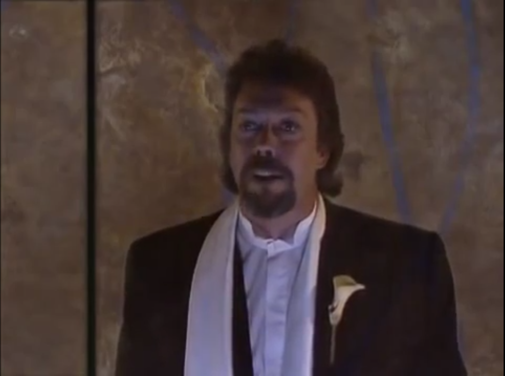 Tim Curry wearing a nice dinner jacket, white shirt, white scarf and an Arum-lily on his lapel.