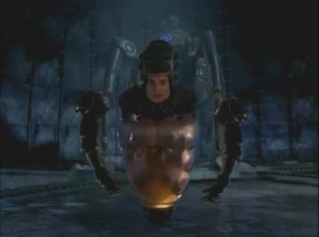  A man's head floating on top of a murky triangular jar with 2 robotic floating arms flanking him. 