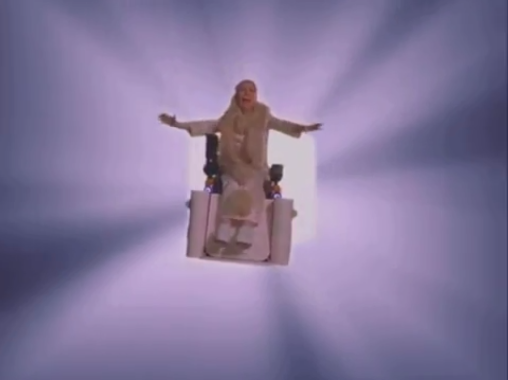 An old woman in a wheelchair floating in the middle of the screen as a white void opens behind her.